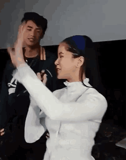 a woman in a white dress is dancing in front of a man in a green jacket .