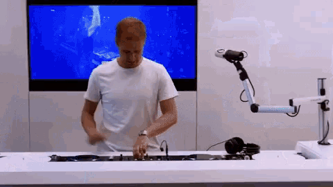 a man in a white shirt is playing a dj set in front of a large screen