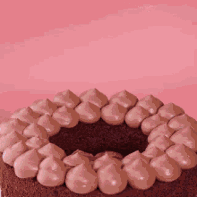 a close up of a chocolate cake with pink frosting on a pink background