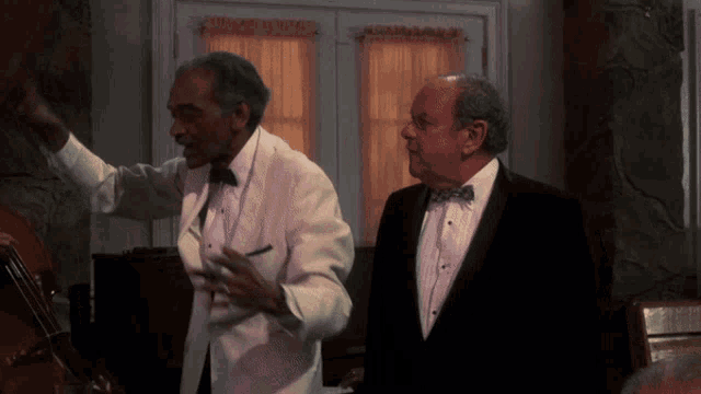 two men in tuxedos are standing in front of a window