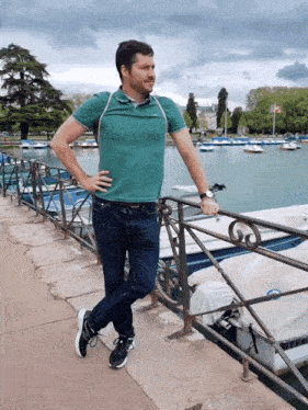 a man in a green shirt leans on a railing in front of boats