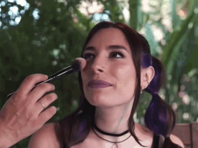 a woman with purple hair is being brushed on her face