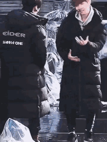 a man in a black jacket with the word eider on the back is standing in the rain holding an umbrella .