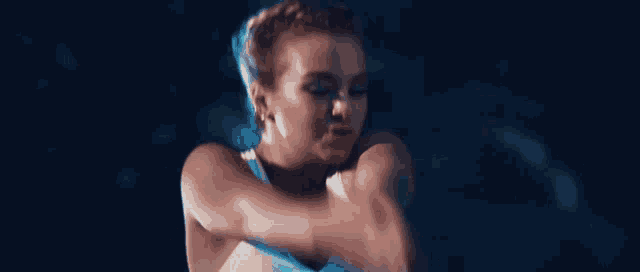 a woman is dancing in a dark room with a blue light behind her .