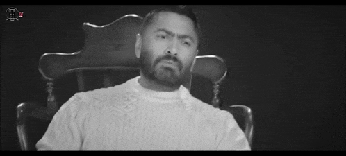 a man with a beard is sitting in a chair wearing a white sweater .