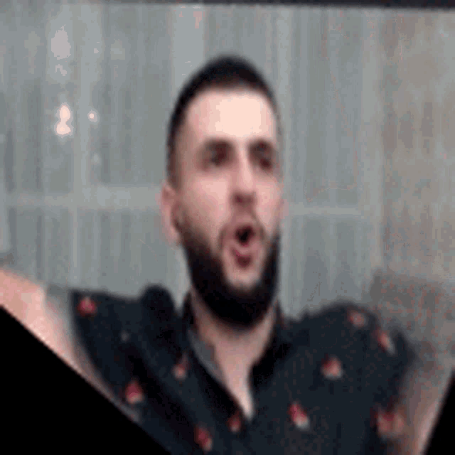 a man with a beard is wearing a black shirt with red flowers on it