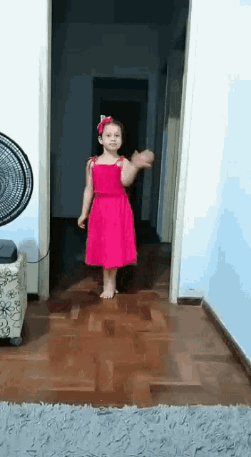 a little girl in a pink dress is standing in a hallway .