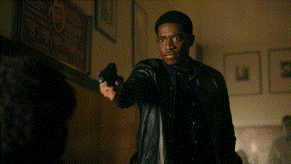 a man in a black leather jacket is pointing a gun at another man .