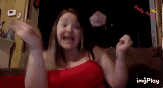 a woman in a red top is making a funny face with her hands in the air