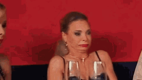 a woman is making a funny face while sitting at a table with wine glasses .