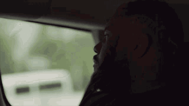 a man is sitting in the back seat of a car looking out the window .