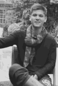 a man wearing a scarf is sitting in front of a sign that says los mayar