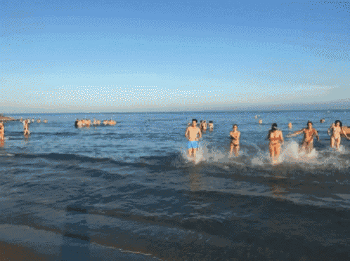 a group of people are running into the ocean on a beach