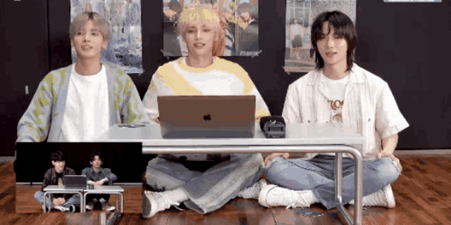 three young men sit on the floor with their legs crossed in front of a laptop