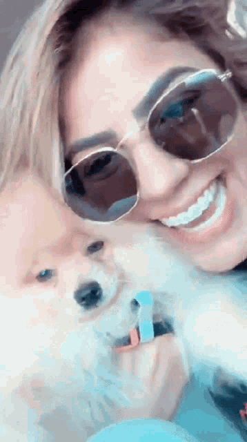 a woman wearing sunglasses is smiling while holding a small dog