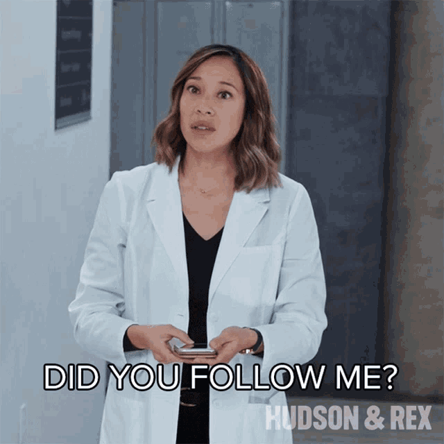 a woman in a lab coat is holding a cell phone and asking if she should follow her