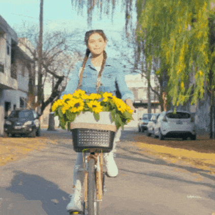a woman is riding a bike with a basket of yellow flowers
