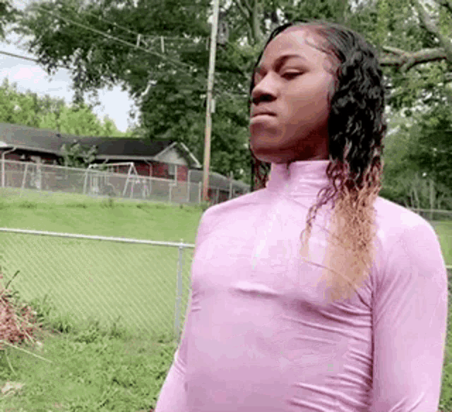 a woman in a pink shirt is standing next to a chain link fence .
