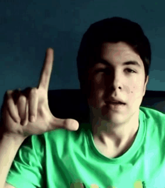 a young man in a green shirt is making a hand gesture with his finger