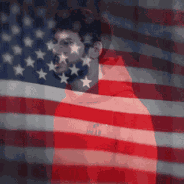 a man in a red hoodie stands in front of a large american flag