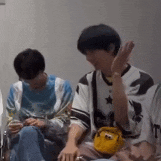 a group of young men are sitting next to each other in a room and one of them is holding a yellow bag .