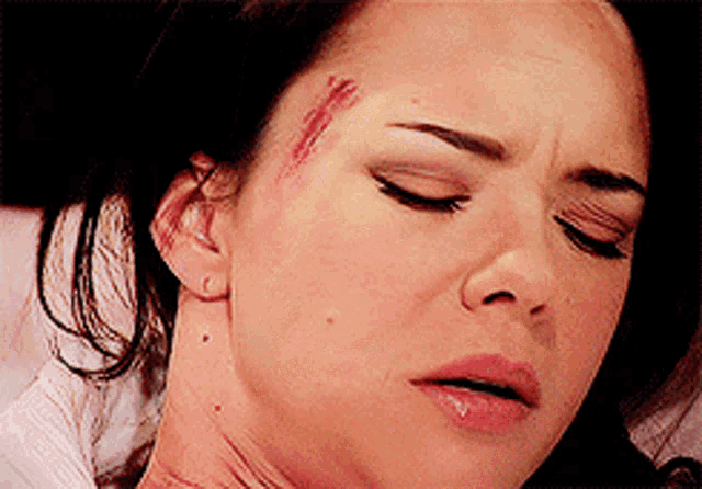 a close up of a woman 's face with a bloody wound on her forehead