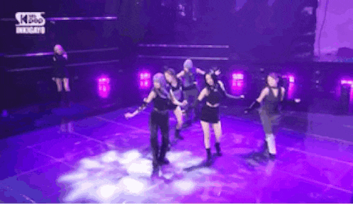 a group of women are dancing on a stage with purple lights behind them .