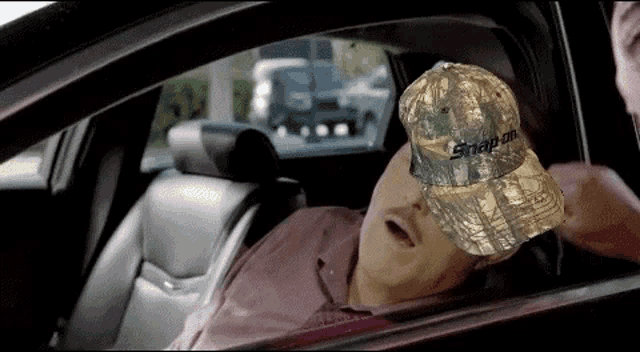 a man wearing a snap on hat is sleeping in the back seat of a car .