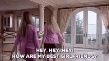 two women are standing in a living room holding hands and talking .