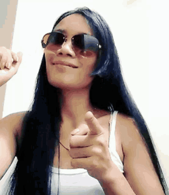 a woman wearing sunglasses is pointing at the camera