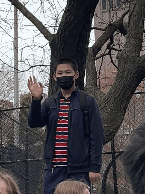 a young man wearing a mask and a striped shirt is waving his hand