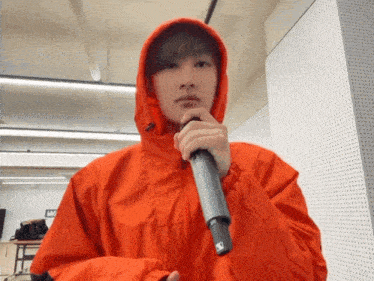 a man in an orange jacket is holding a microphone in front of a wall with the letter w on it
