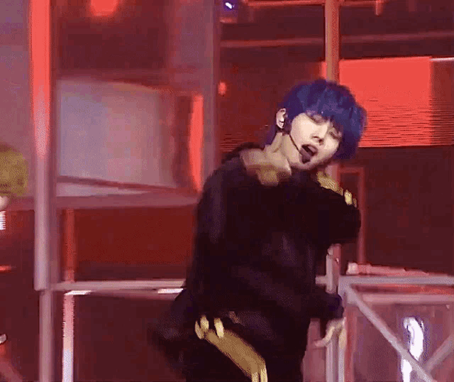 a man with blue hair is dancing on a stage with a microphone in his mouth .