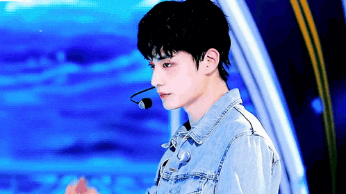 a young man wearing a denim jacket and a microphone is standing in front of a blue background .