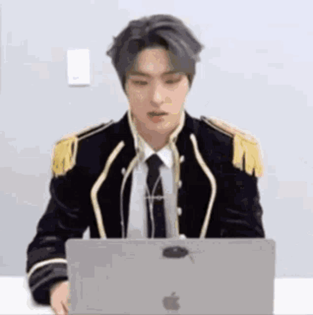a man in a suit and tie is sitting at a table using an apple laptop computer .