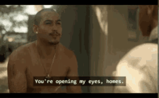 a man without a shirt is talking to another man while sitting in front of a mirror .