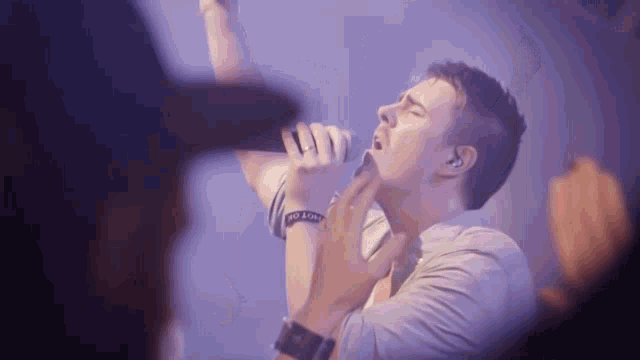 a man is singing into a microphone with a wristband that says no love on it .