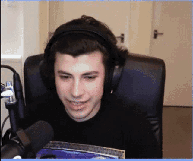 a young man wearing headphones and a black shirt is sitting in front of a microphone .