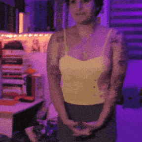 a woman with tattoos on her arms is standing in a room with purple lights