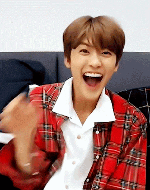 a young man wearing a plaid shirt is sitting on a couch with his mouth open