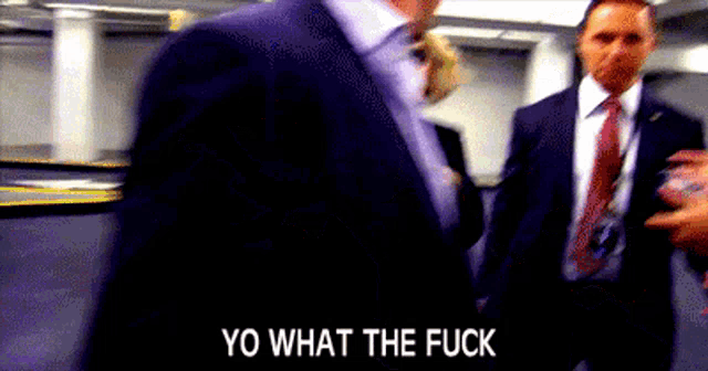 a man in a suit and tie is standing next to another man and says yo what the fuck .