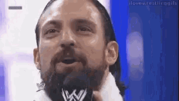 a man with a beard is talking into a microphone while wearing a white shirt .