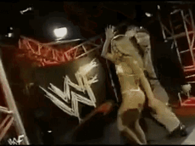 a woman in a bikini is standing next to a man in a wrestling ring in front of a w logo .
