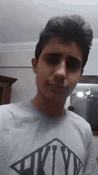 a young man wearing a grey shirt with a black superman logo on it
