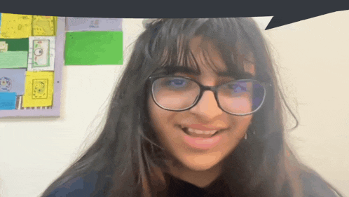 a girl wearing glasses is smiling in front of a bulletin board that says " i love you "