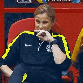 a woman wearing a black and yellow nike jacket is sitting in a red chair .