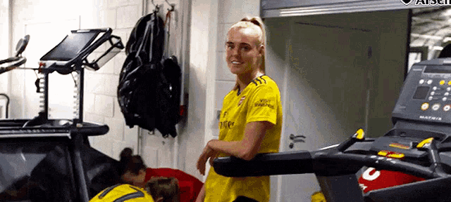 a woman in a yellow shirt is standing on a treadmill with the number 3 on it