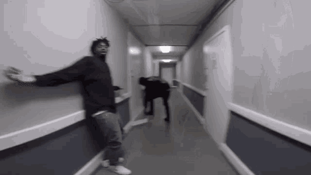 a man is standing in a hallway with his arms outstretched while another man stands behind him .