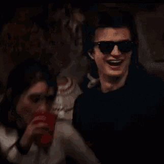 a man wearing sunglasses is drinking from a red cup while a woman looks on .
