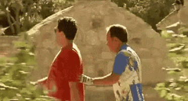 two men are standing next to each other in front of a rock .